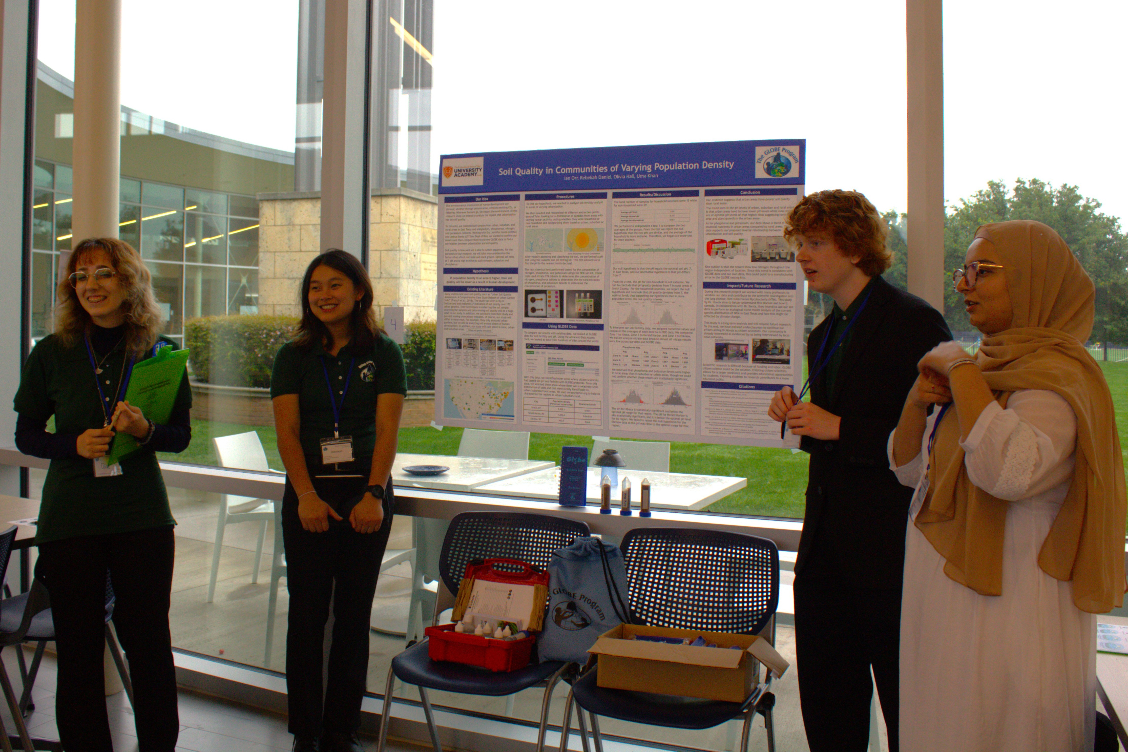 four high school students stand beside their research poster at a student research symposium