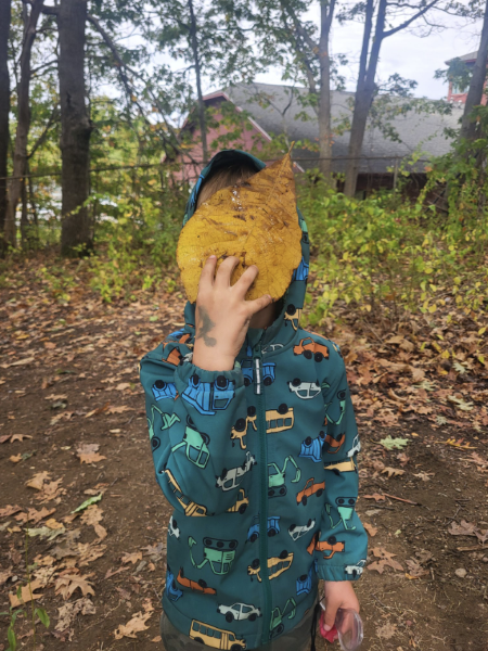 a student holds a large yellow leaf in front of their face; the leaf covers their entire face!